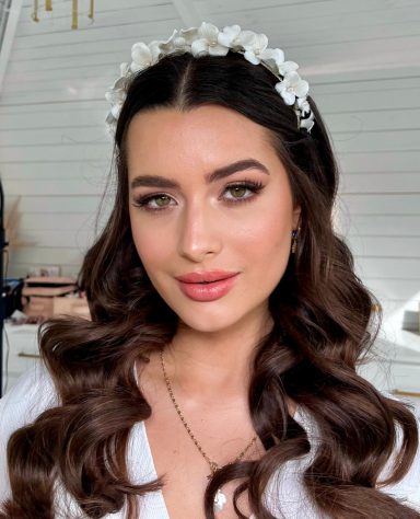 Woman with wavy brown hair, soft glam makeup, and neutral tones.